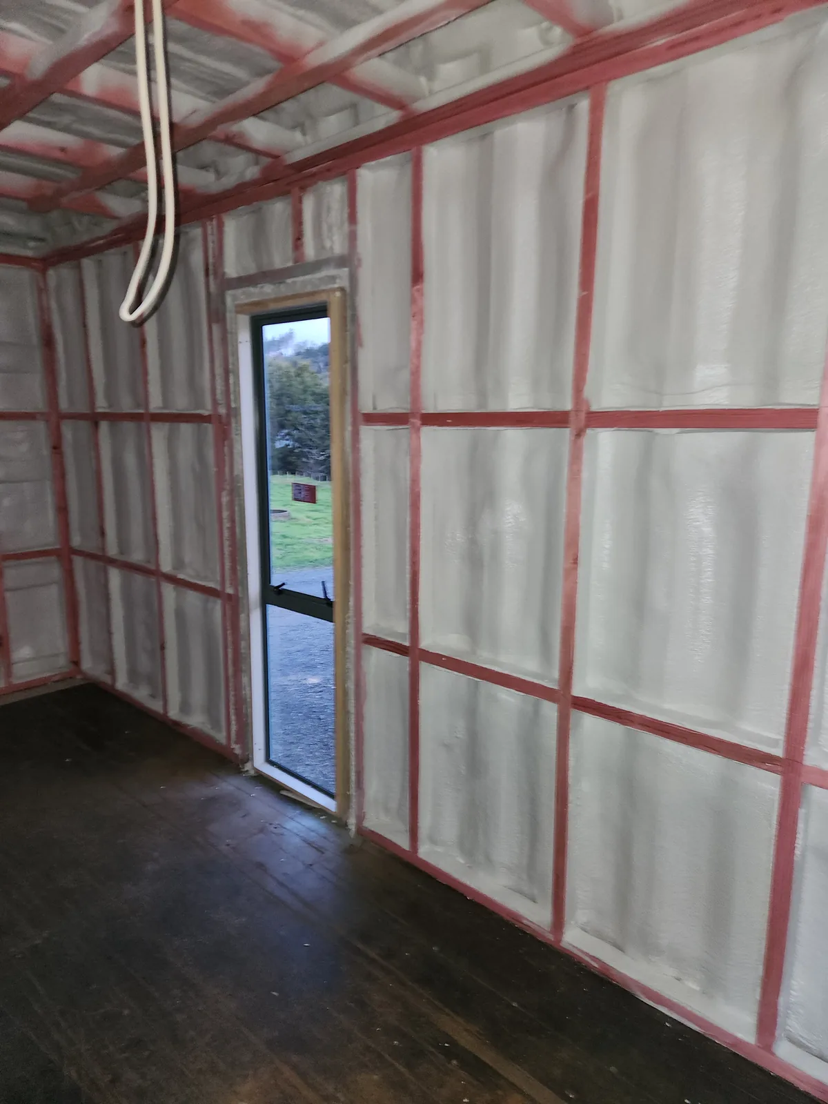 Closed-cell spray foam insulation installed around container framing and a doorway before internal lining